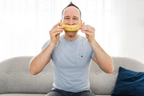 divertente banana man sorridente sul divano - men banana holding cut out foto e immagini stock