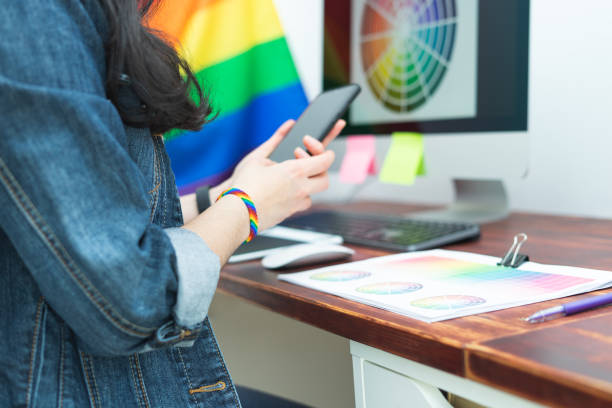 femme dans le bureau avec le téléphone portable et les accessoires lgbt et le drapeau gay. culture lgbtqia. - homosexual gay pride business rainbow photos et images de collection