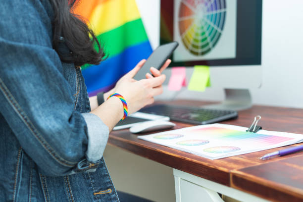 donna in ufficio con cellulare e accessori lgbt e bandiera gay. cultura lgbtqia. - gay pride wristband rainbow lgbt foto e immagini stock