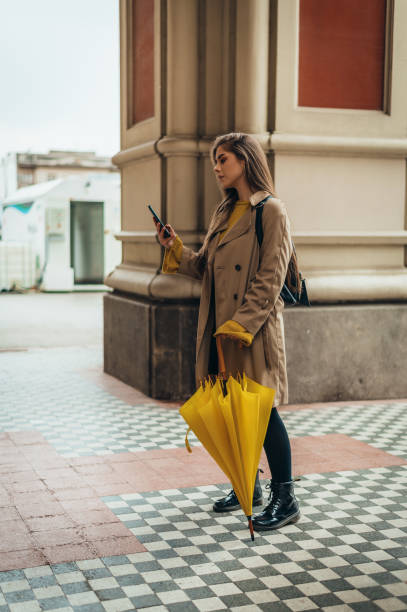 istock Woman using smartphone and holding a yellow umbrella 1313887928