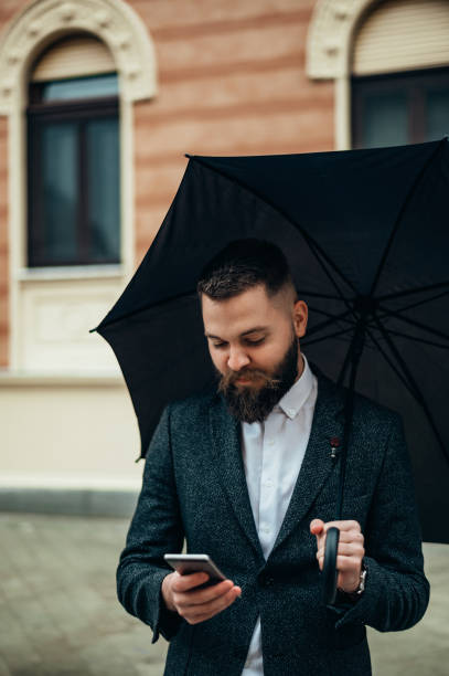 istock Businessman using a smartphone and holding a black umbrella 1313888002
