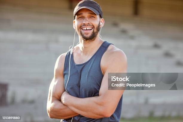 Shot Of A Sporty Young Man Wearing His Earphones And Standing With His Arms Crossed Outside Stock Photo - Download Image Now