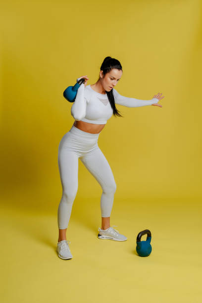 istock Image of young attractive female doing kettle bell exercise on yellow background. 1313896388