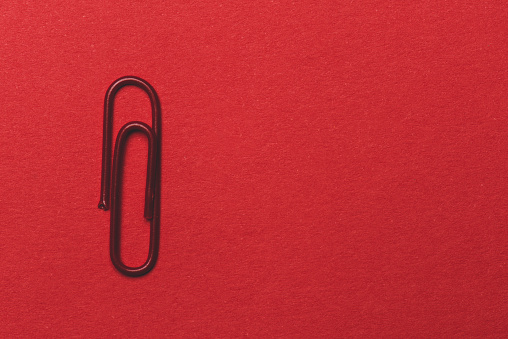 Red paper clip over the red background.