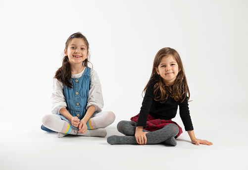 Two little girls sitting on the white background.