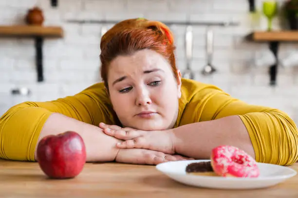 Photo of Sad woman choosing between sweets and fruits, healthy eating and junk food. The choice. Two options. The choice between eating. Delema, for a healthy lifestyle or not.