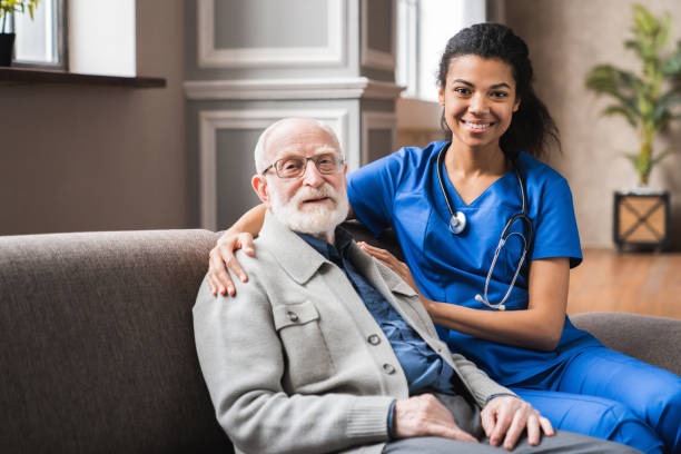 Front view portrait of caring afro nurse taking care of an elderly caucasian man grandfather grandpa indoors. Happy female doctor consulting old man in clinic. Front view portrait of caring afro nurse taking care of an elderly caucasian man grandfather grandpa indoors. Happy female doctor consulting old man in clinic. assistant stock pictures, royalty-free photos & images