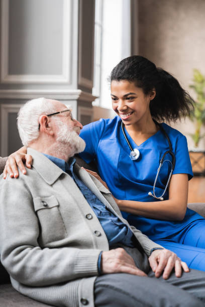 foto verticale di utile giovane infermiera medico che consulta l'anziano vecchio . uomo anziano anni '80 che parla di condizioni di salute e medicina con la donna medico generico. - male nurse black nurse doctor foto e immagini stock