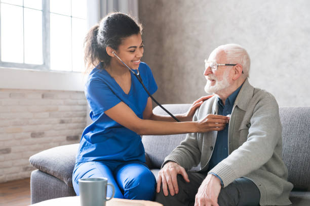 female attending physician holding stethoscope listening old patient during homecare visit. doctor checking heartbeat examining elder retired man at home. seniors heart diseases, cardiology concept. - home health nurse imagens e fotografias de stock