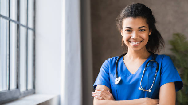병원 배경에 청진기를 가진 아프리카 계 미국인 여성 의사의 초상화. 쾌활한 몸짓으로 서 있는 의사. 여자 간호사는 웃는 얼굴로 의사 유니폼을 입고 있습니다. 건강 보험 및 의사 개념. - 간호사 뉴스 사진 이미지
