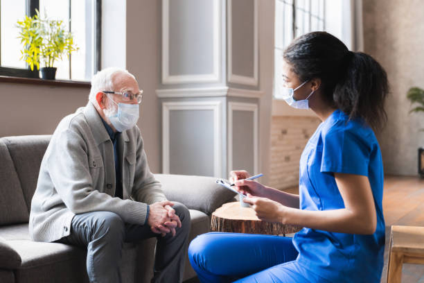 jeune docteur africain de femme donnent une consultation au vieil homme aîné de grand-père pendant la visite à la maison dans le masque médical contre covid 19. infirmière de femme visite le patient masculin aîné à la maison consultent au sujet de - physical injury men orthopedic equipment isolated on white photos et images de collection