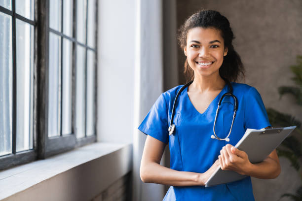 médico afro-americano que trabalha em hospital, saúde e conceito médico. estetoscópio em volta do pescoço dela. médica negra do sexo feminino preenchendo formulário médico na prancheta enquanto estava em pé no hospital - estágio - fotografias e filmes do acervo