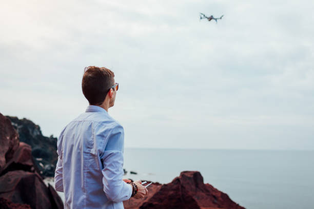 Drone remote control. Man operating copter controller by sea. Aerial video shooting of Red beach on Santorini island