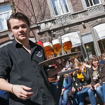 Maastricht, Limburg, Netherlands, april 20th 2013, a waiter walking with a tray of beer, serving people that are enjoying the beautiful weather on their free Saturday at a sidewalk cafe on the \