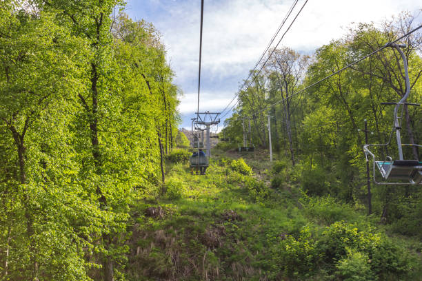 Chairlift in the mountains. Ascent on a cableway among green trees. Tourist mountain resort. Spring landscape. Climbing to the top.