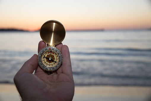 A person holding a small golden compass at the beach. Heading concept