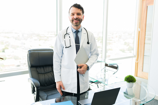 Happy doctor doing a rewarding job. Medical specialist smiling and getting ready to receive a new patient in his modern office