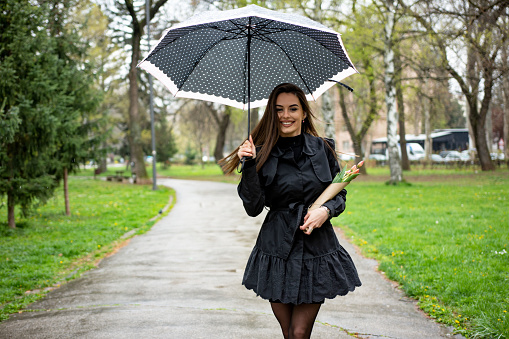 Beautiful young woman with tulips bouquet and umbrella in the park
