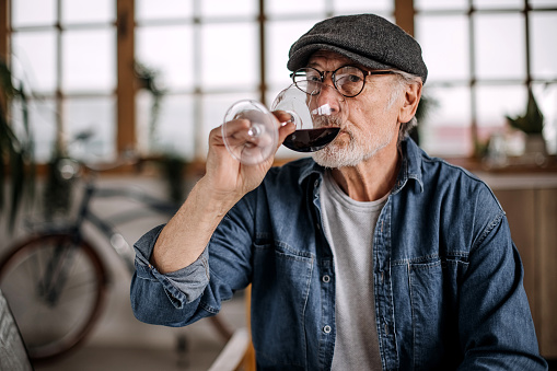 Senior man enjoying glass of wine at the comfort of his apartment