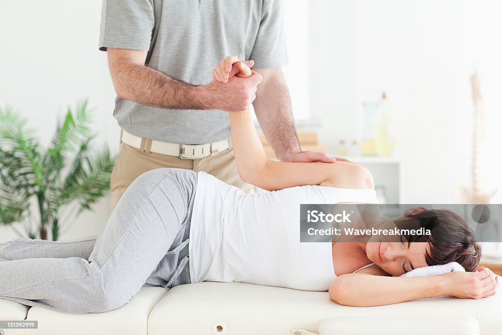 Chiropractor stretches female customer's arm A chiropractor stretches a female customer's arm in his surgery Active Lifestyle Stock Photo