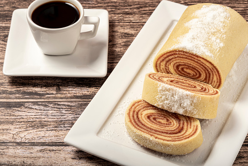 Roll cake and coffee on a table.