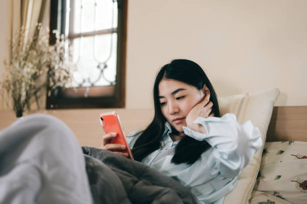 joven adulta soltera usando teléfono inteligente en la cama. - working bed smart phone bedroom fotografías e imágenes de stock