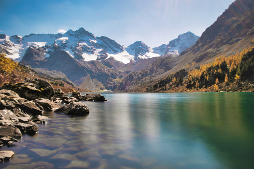 The autumn landscape of mountain lake surrounded by snow peaks at sunny day. Long exposure photo.