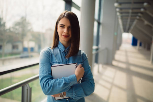 istock Beautiful brunette is holding notebook in her hands while standing in corridor 1313952864