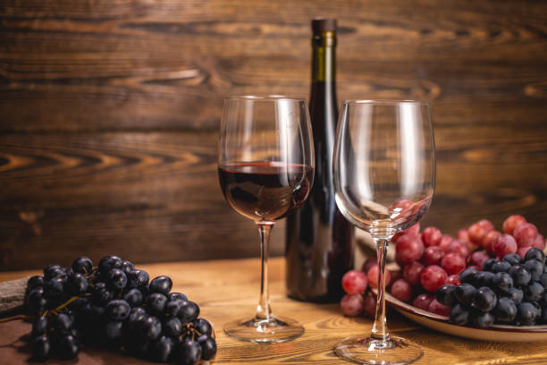 Bottle of dry red wine with a glass and a bunch of grapes on a wooden table. Concept of viticulture and winemaking stock photo