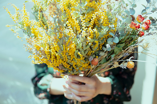 Close-up photo of a woman with a bouquet of dried flowers surrounded by plants