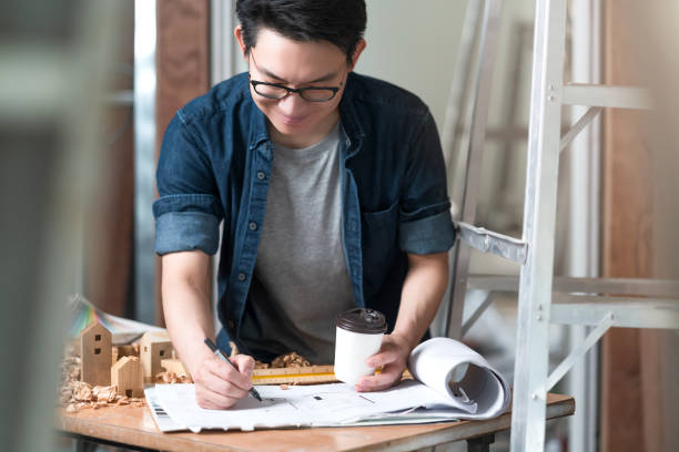 istock asian attractive glasses interior designer working at house site renovation construction progress with smile and confident at desk with blue print and drawing tool 1313959558