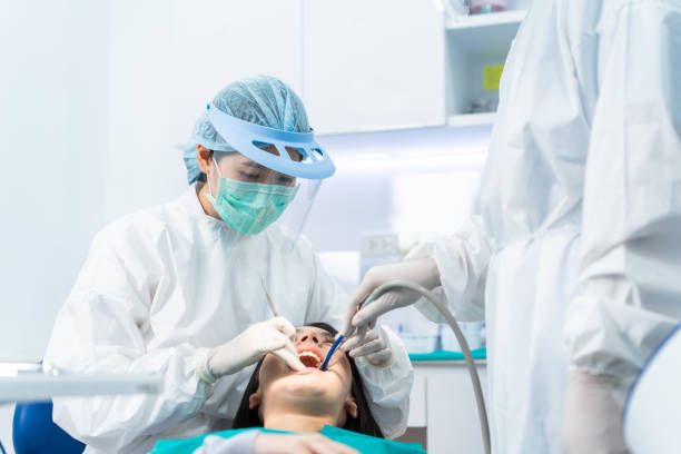 asiatische fachzahnarzt arzt tragen psa und maske untersuchen patienten zähne in der zahnklinik. dentalassistentin verwenden saugung, um den mund des jungen mädchens trocken zu halten due treatment procedures during coronavirus pandemic - caucasian cavity clinic color image stock-fotos und bilder