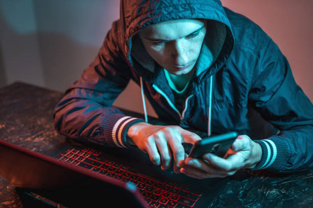 istock Hacker with phone is typing on a laptop keyboard in a dark room under a neon light. Cybercrime fraud and identity theft 1313967084
