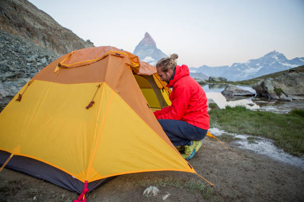 istock Man prepares tent for camping on mountain top, Matterhorn view 1313974569