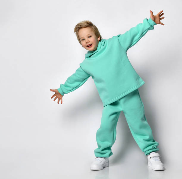 istock Happy cute blond boy in a warm turquoise suit on a gray background 1313974589
