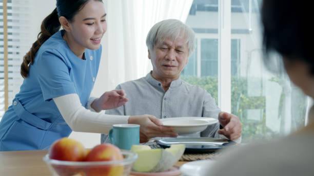 매력적인 젊은 아시아 시민 부부는 행복한 앉아서 이야기하고, 오래된 아시아 요양원에서 일상적인 라이프 스타일로 아침에 집에서 식탁에서 건강한 영양 아침 식사를 위해 수프를 먹습니다. - senior adult nursing home eating home interior 뉴스 사진 이미지