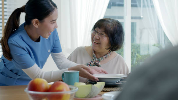 魅力的な若いシニアアジア市民カップル幸せな座って、話し、古いアジアの看護のホームケアの日常的なライフスタイルで、朝自宅のダイニングテーブルで健康的な栄養朝食の食事のための� - senior adult nursing home eating home interior ストックフォトと画像