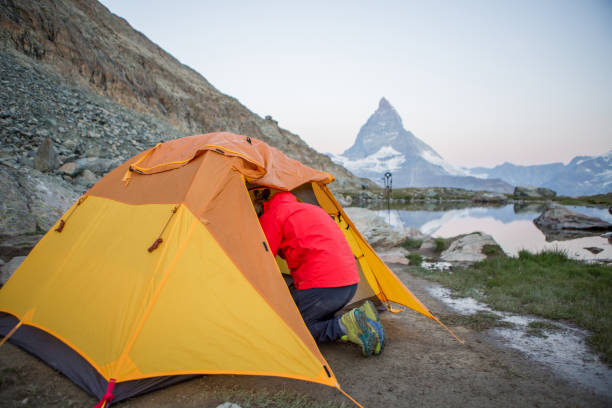 istock Man prepares tent for camping on mountain top, Matterhorn view 1313975131