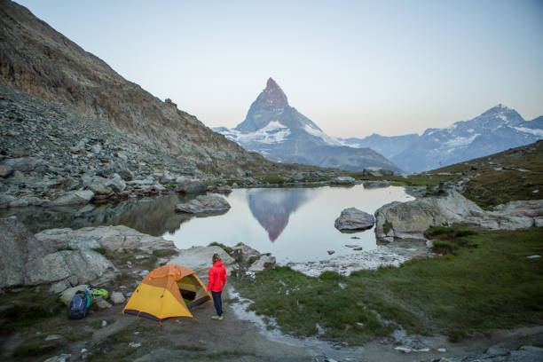 istock Man prepares tent for camping on mountain top, Matterhorn view 1313975851
