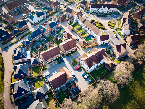 Aerial view taken by drone depicting a brand new housing estate and construction - new houses are still being built on the site - site from above. The rows of houses include terraced housing and detached, with pristine green lawns and gardens.