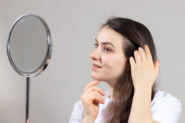 une femme brune de 20-30 ans se regarde dans le miroir et s’admire. amour de soi, soins de la peau et des cheveux du visage, . peau saine du visage pour la publicité en dermatologie et cosmétologie - cosmetics young women human skin 25 30 years photos et images de collection