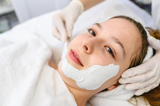 Cosmetologist doing cosmetic face mask treatment for the young woman