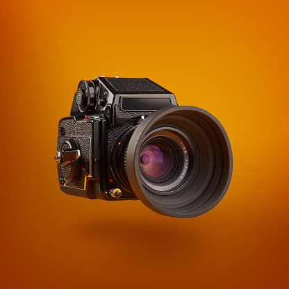 Medium format film camera flowating over an orange colored background