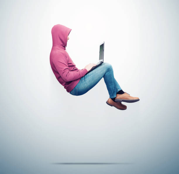 A man in a red sweatshirt, jeans levitates in the air working on a laptop, on blue background. Side view. Computer superiority concept A man in a red sweatshirt, jeans levitates in the air working on a laptop, on blue background. Side view. Computer superiority concept levitation photos stock pictures, royalty-free photos & images