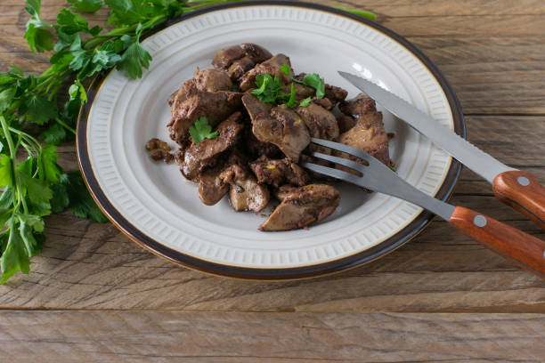 Cooked chicken liver with onion on a plate served on wooden desk. Rustic style.