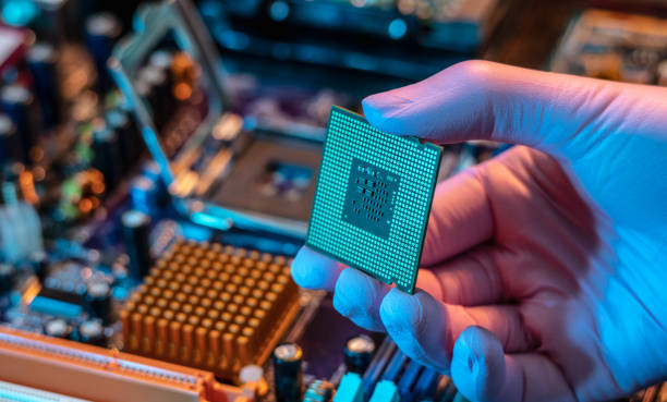 инженер в перчатках держит чип процессора на фоне материнской платы. высокотехнологичная аппаратная микроэлектроника - cpu socket стоковые фото и изображения
