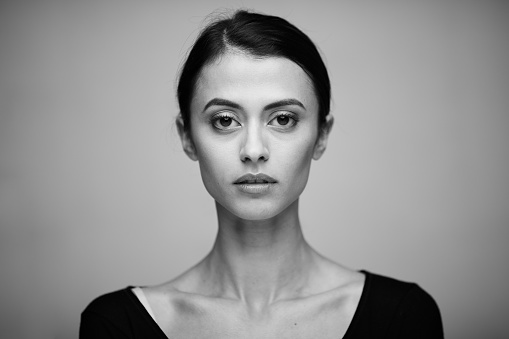 Black and white portrait of a beautiful elegant professional woman standing with folded arms in a stylish jacket looking at the camera with an enigmatic smile, with copy space