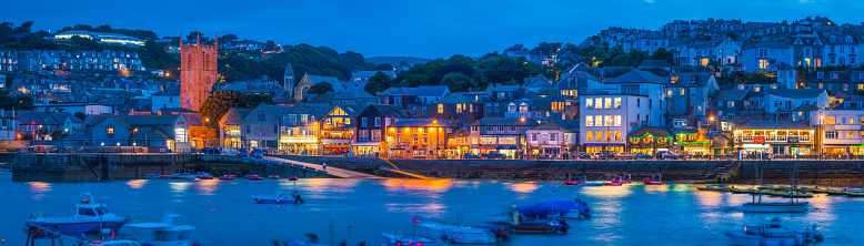 Panoramic view across the ocean bay of St. Ives to the warm glow of the quayside shops, pubs and restaurants around the famous harbour.