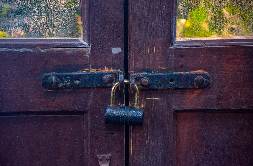 A fragment of an old brown battered door, padlocked.
