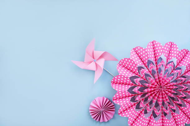 Pink flower made of paper and paper windmill on light blue background.